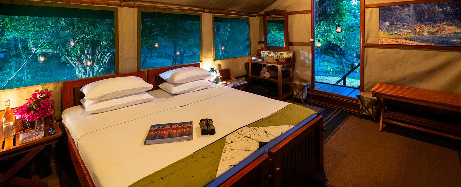 Inside a tent: a double bed, a desk and screened windows onto green trees